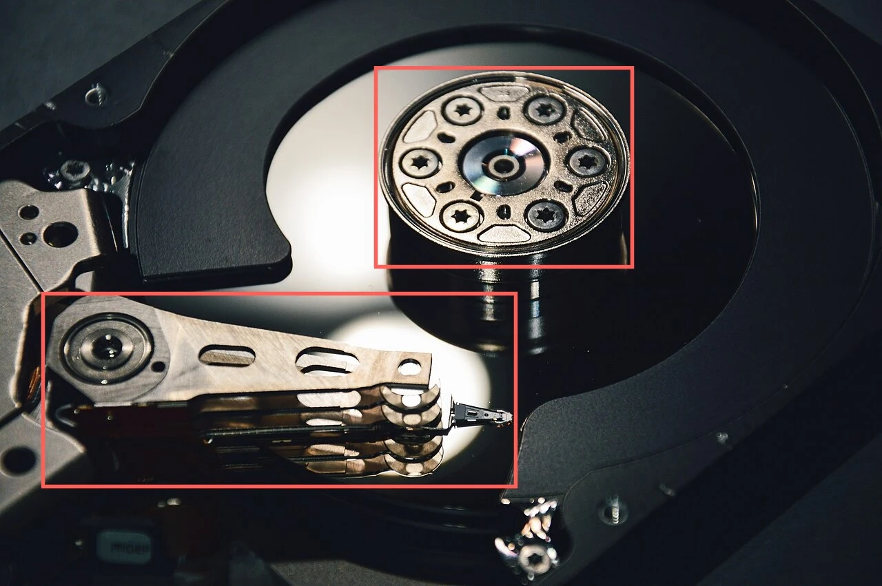 A hard disk drive with its lid removed: a mirror-finish round platter with a metal hub at its centre, and a long metal arm lying across the lower left. A red box surrounds the hub and a second red box surrounds the arm