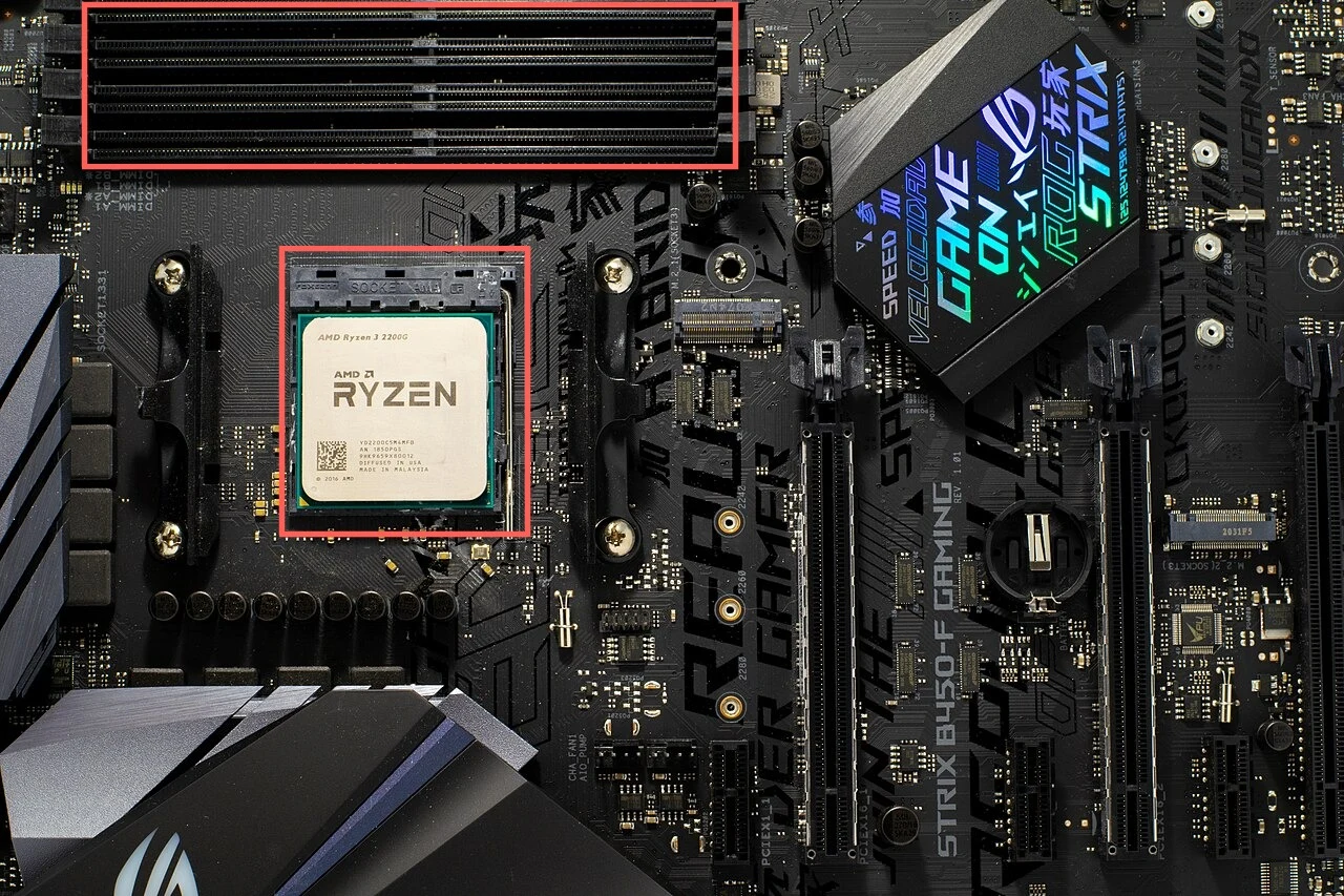 A mostly black desktop motherboard seen from above. A red box at the top surrounds four long memory slots, and a second red box in the middle surrounds a square CPU socket with a processor fitted in it. Two long expansion slots run down the lower right