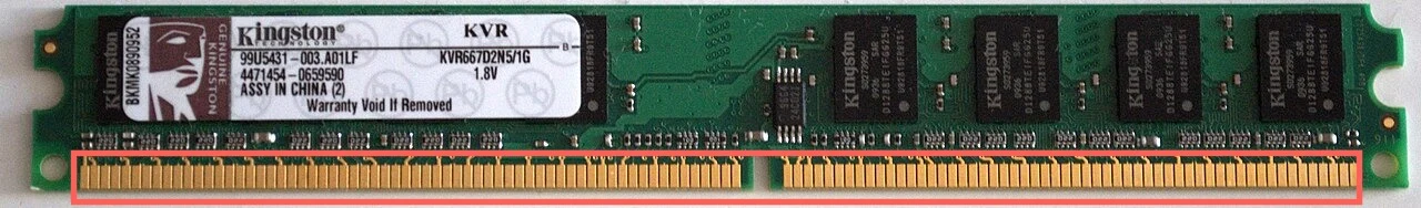 A desktop memory module lying flat: a green circuit board with a white label at the left, several black memory chips along its length, and a row of gold contacts along the bottom edge with a gap near the middle. A red box surrounds the gold contacts