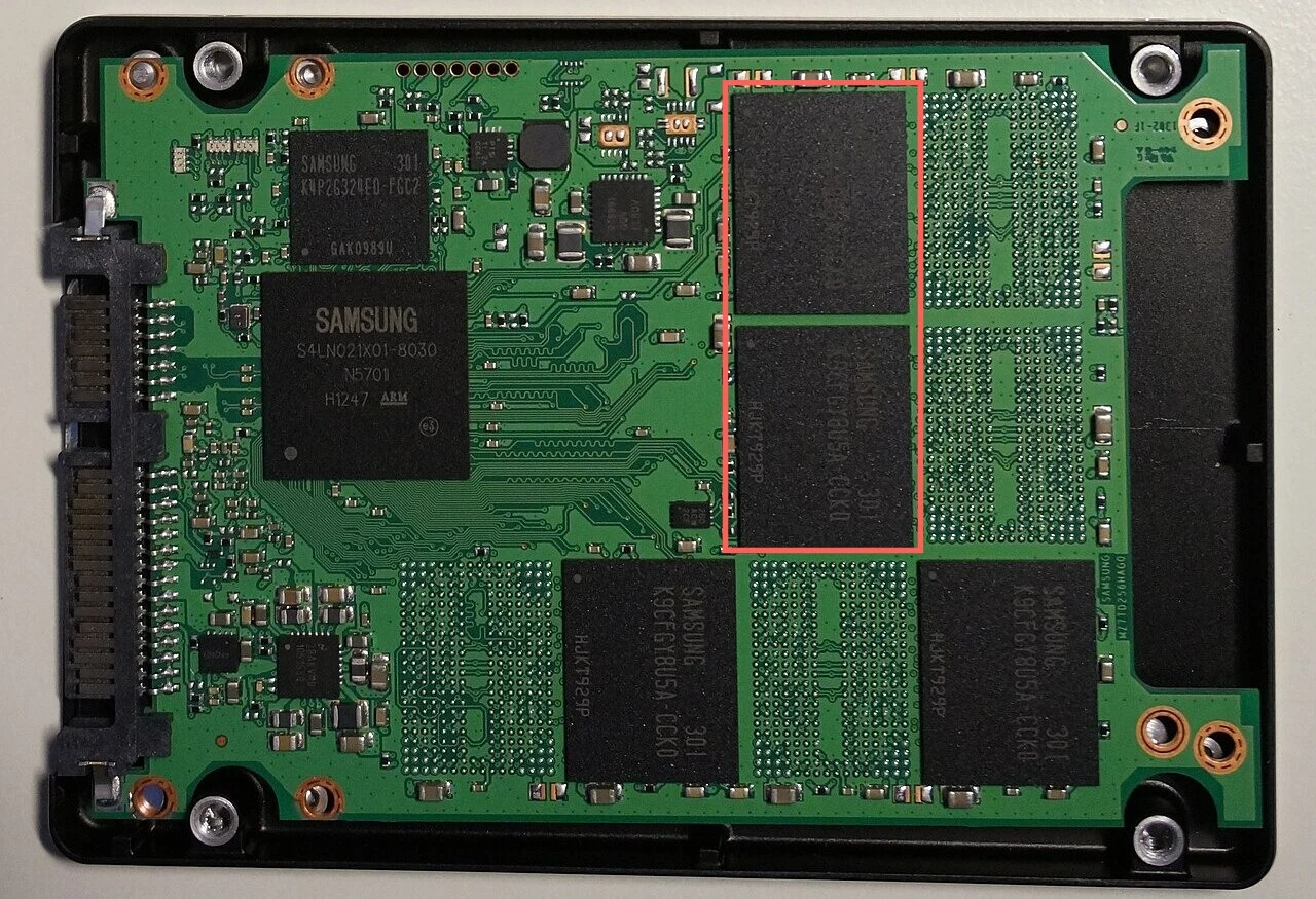 The green circuit board of a 2.5-inch solid-state drive with its cover removed, with a connector at the left, a large controller chip and several black flash memory chips. A red box surrounds two of the flash chips